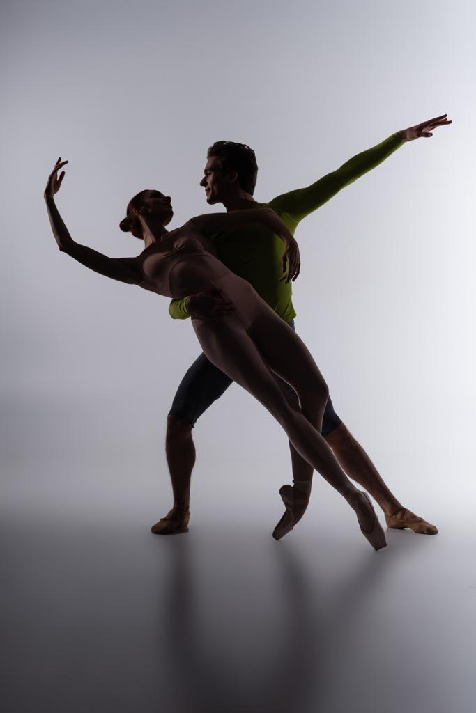 Silhouette einer Balletttänzerin, die eine Ballerina auf dunkelgrau unterstützt - Foto, Bild