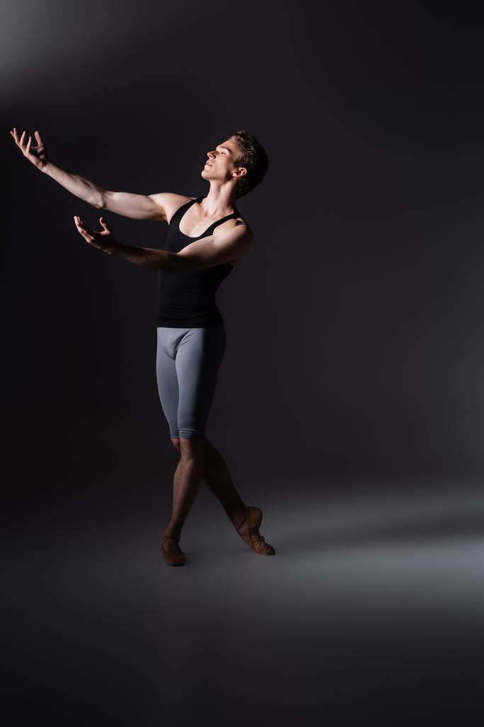 pełna wdzięku tancerka z wyciągniętymi rękami wykonująca taniec baletowy na czarno - Zdjęcie, obraz