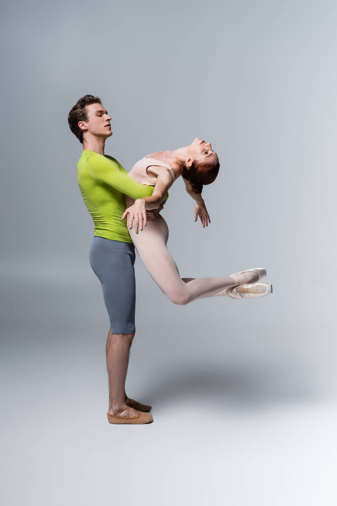 сильная балерина, поднимающая балерину в телесном костюме на сером - Фото, изображение
