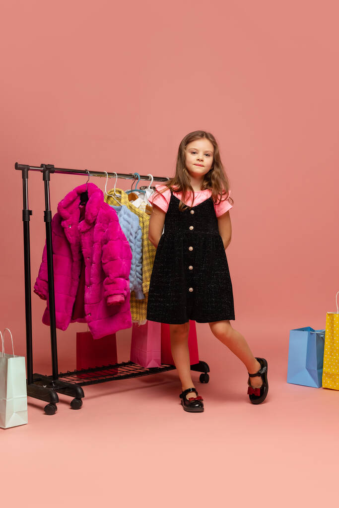 Όμορφο κοριτσάκι, χαριτωμένο παιδί διαλέγει ρούχα, φόρεμα σε κατάστημα ρούχων. Συναισθήματα, μαύρη Παρασκευή, αγορές, έκπτωση, διαφήμιση. - Φωτογραφία, εικόνα