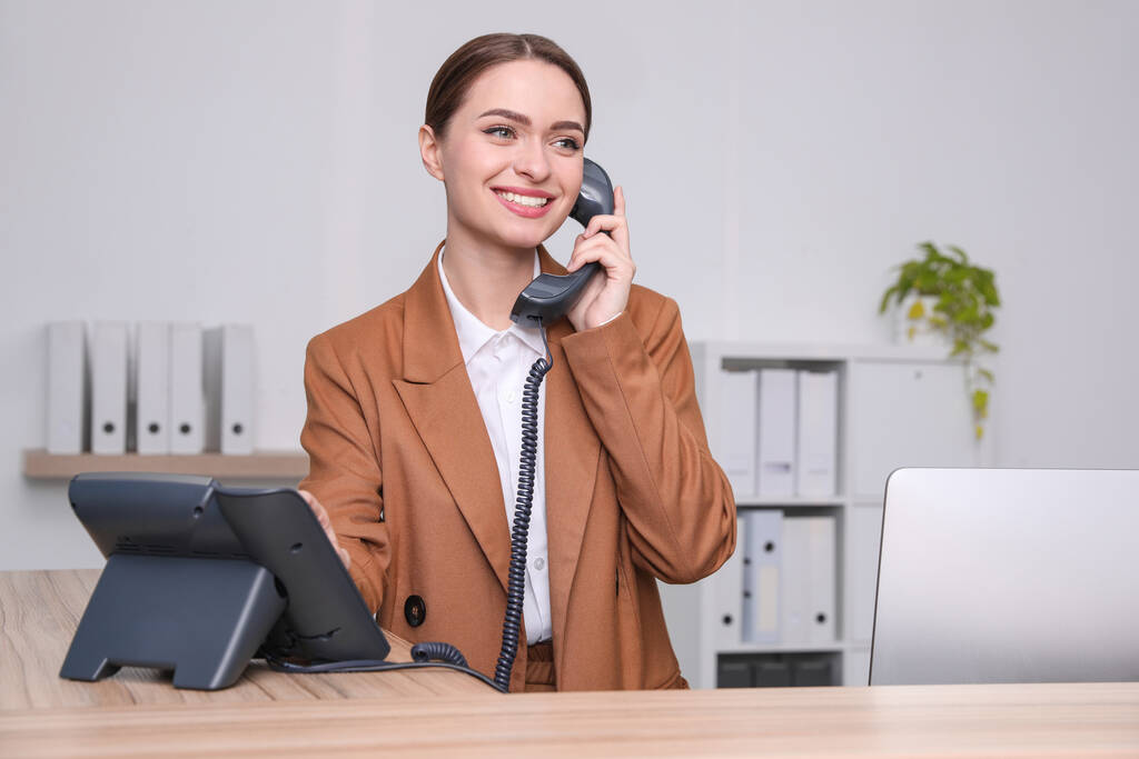 Γυναίκα ρεσεψιονίστ μιλάει στο τηλέφωνο στο χώρο εργασίας - Φωτογραφία, εικόνα