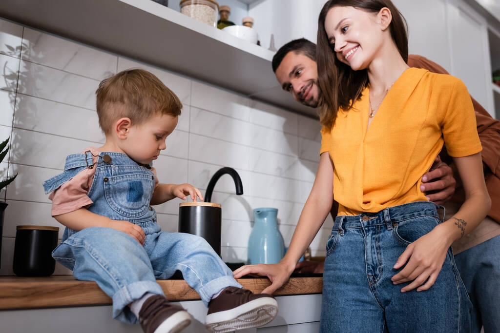 Pikkulapsi istuu keittiön työtasolla lähellä positiivisia vanhempia  - Valokuva, kuva