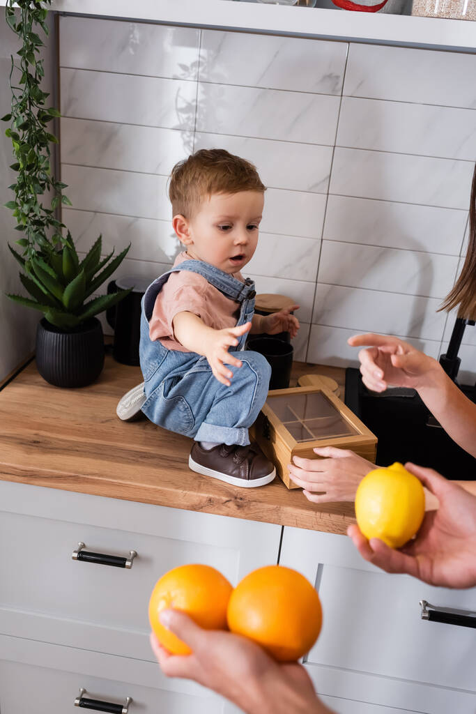 Szülők gazdaság gyümölcsök közelében kisgyermek fia a munkaasztalon a konyhában  - Fotó, kép