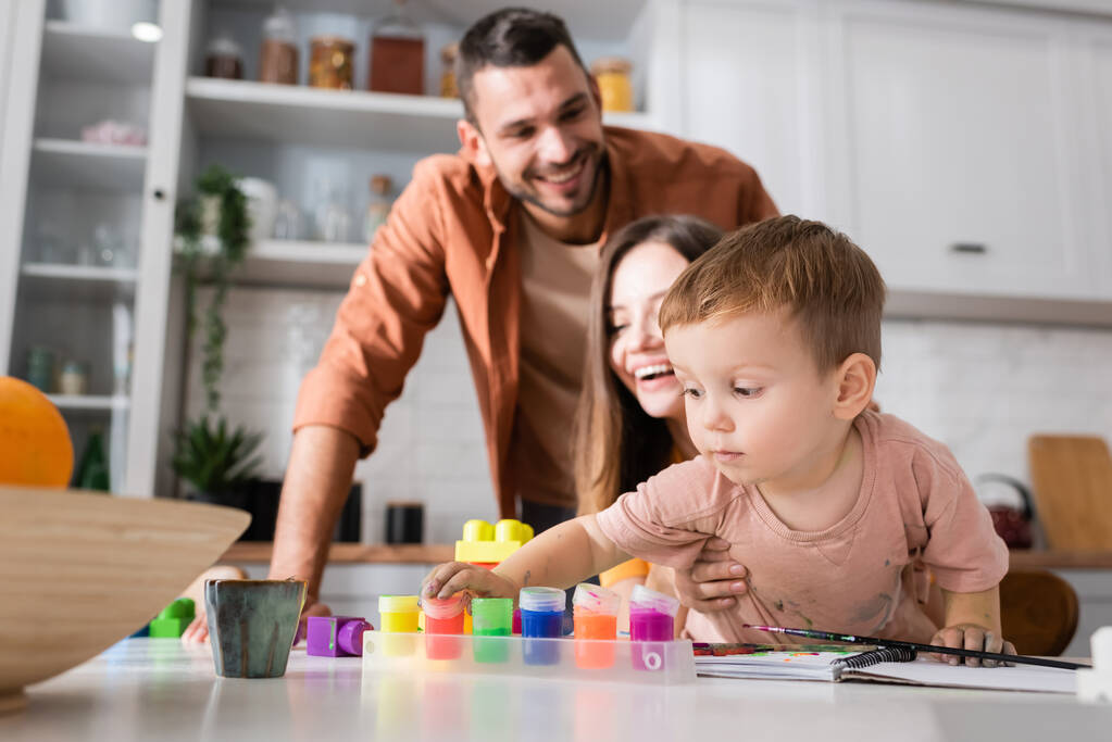Kleinkind nimmt Farbe in der Nähe von Bauklötzen und Eltern zu Hause  - Foto, Bild