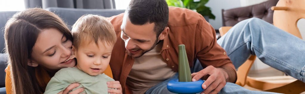 Szczęśliwi rodzice patrząc na syna malucha w pobliżu zabawki w domu, sztandar  - Zdjęcie, obraz