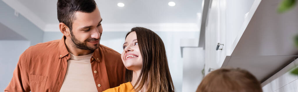Des parents souriants se regardant près d'un enfant flou dans la cuisine, bannière  - Photo, image