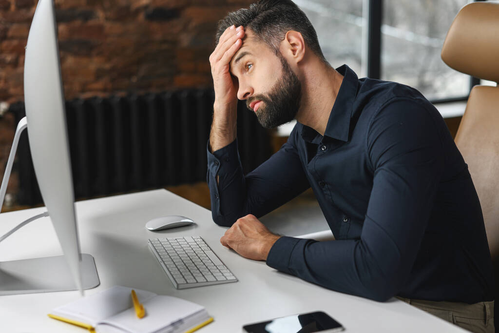 Depressieve jonge mannelijke kantoormedewerker staart naar computer monitor - Foto, afbeelding