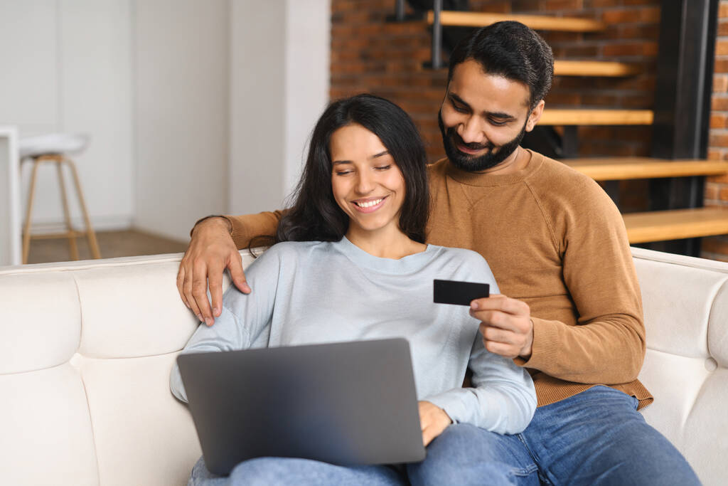 Indiaas koppel kijken op laptop scherm en het controleren van credit card nummer om online transactie te maken. Lachende echtgenoten die online winkelen. Geld overmaken, online bankieren concept - Foto, afbeelding
