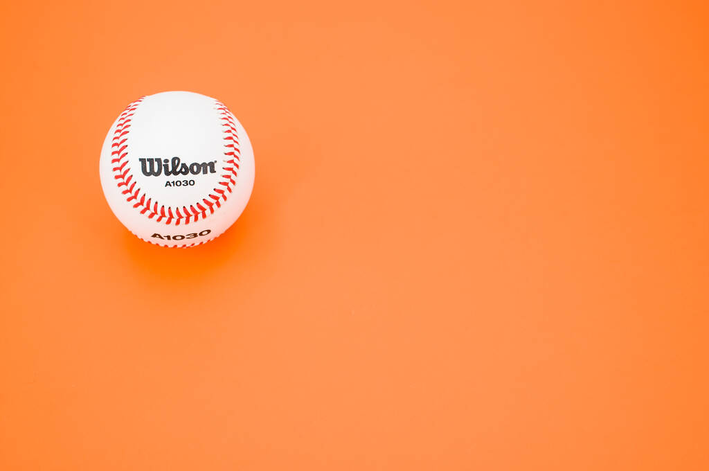 ИНВЕРИГО, ИТАЛИЯ - Дек 08, 2021: изолированный бейсбольный мяч на оранжевом бумажном фоне с текстовым пространством - Фото, изображение