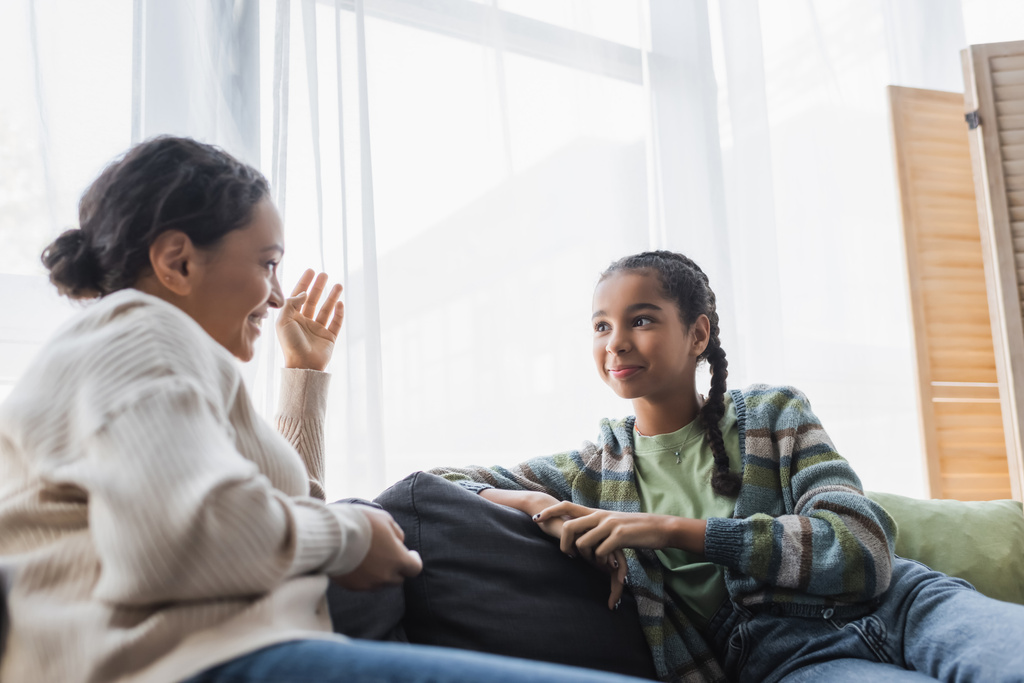 blurred african american woman gesturing while talking to smiling teenage daughter - Photo, Image
