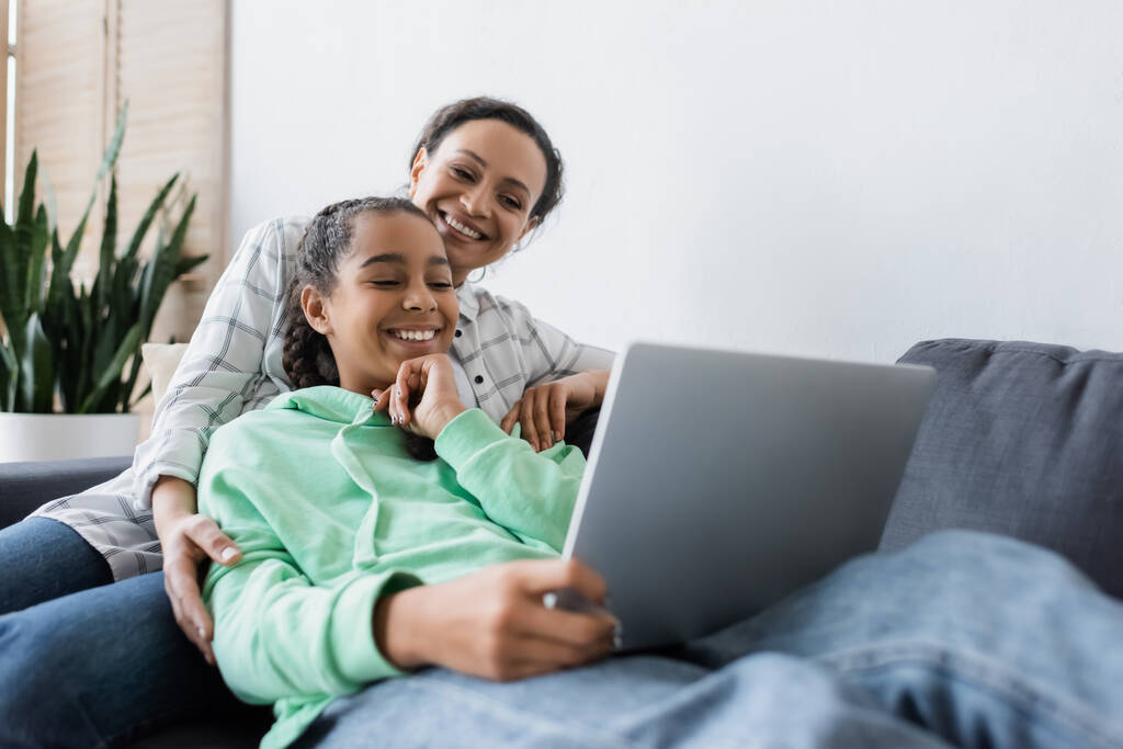 cheerful african american woman with teenage daughter watching film on blurred laptop - Photo, Image