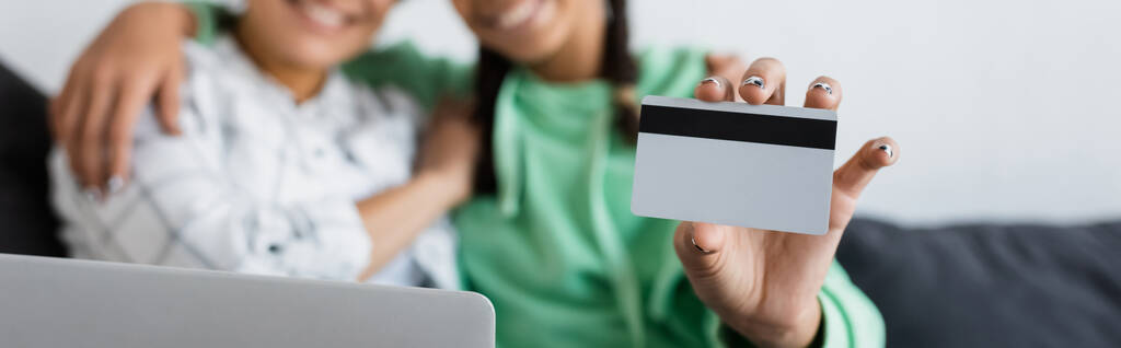 oříznutý pohled rozmazané africké americké dívky držící kreditní kartu v blízkosti notebooku a maminky, banner - Fotografie, Obrázek