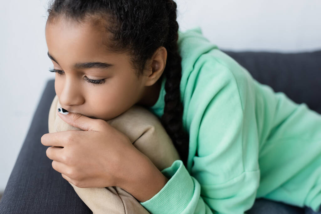 triste Africano americano adolescente menina abraçando travesseiro enquanto deitado em casa - Foto, Imagem