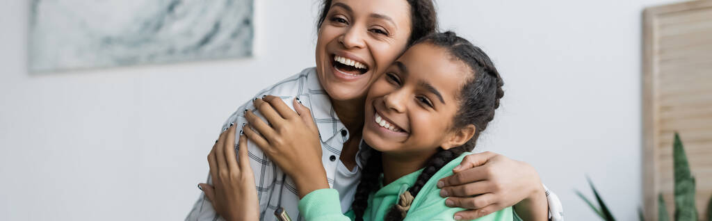 wesoła afrykańska matka i nastoletnia córka przytulają się patrząc w kamerę w domu, sztandar - Zdjęcie, obraz