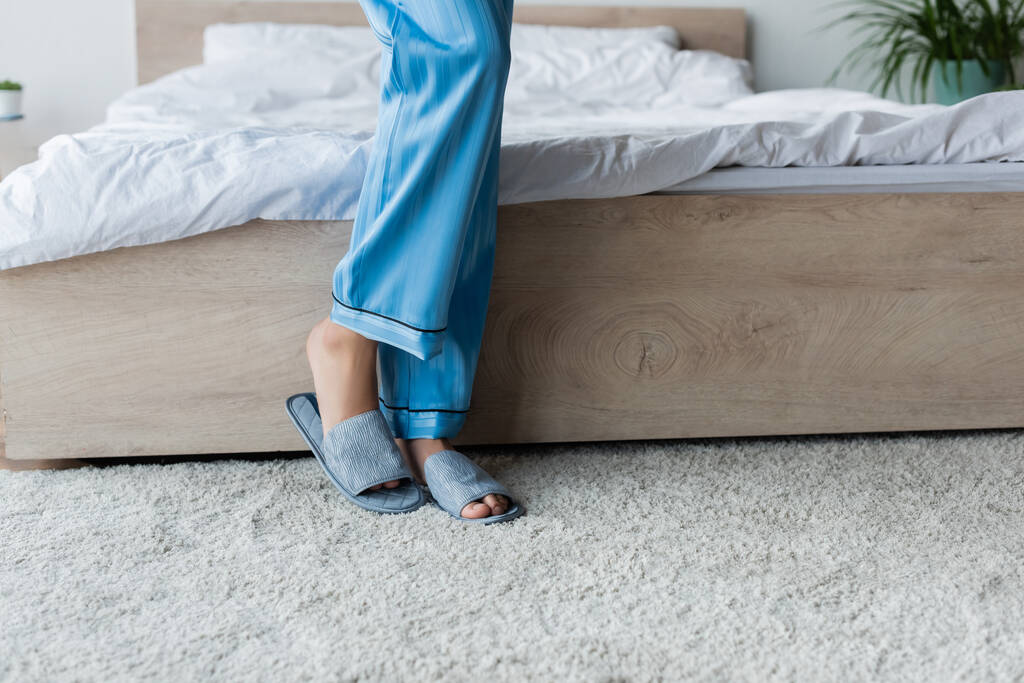 Ausgeschnittene Ansicht einer afrikanisch-amerikanischen Frau in Schlafanzug und Hausschuhen, die neben dem Bett steht - Foto, Bild