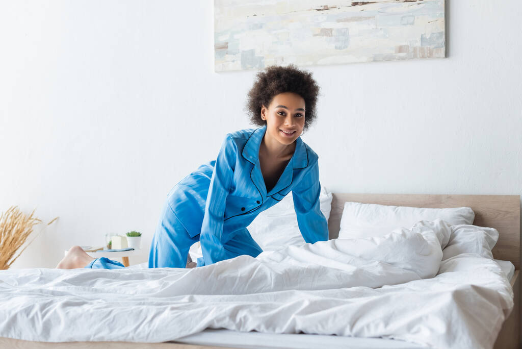 明るい若いアフリカ系アメリカ人女性がベッドでパジャマを着て - 写真・画像