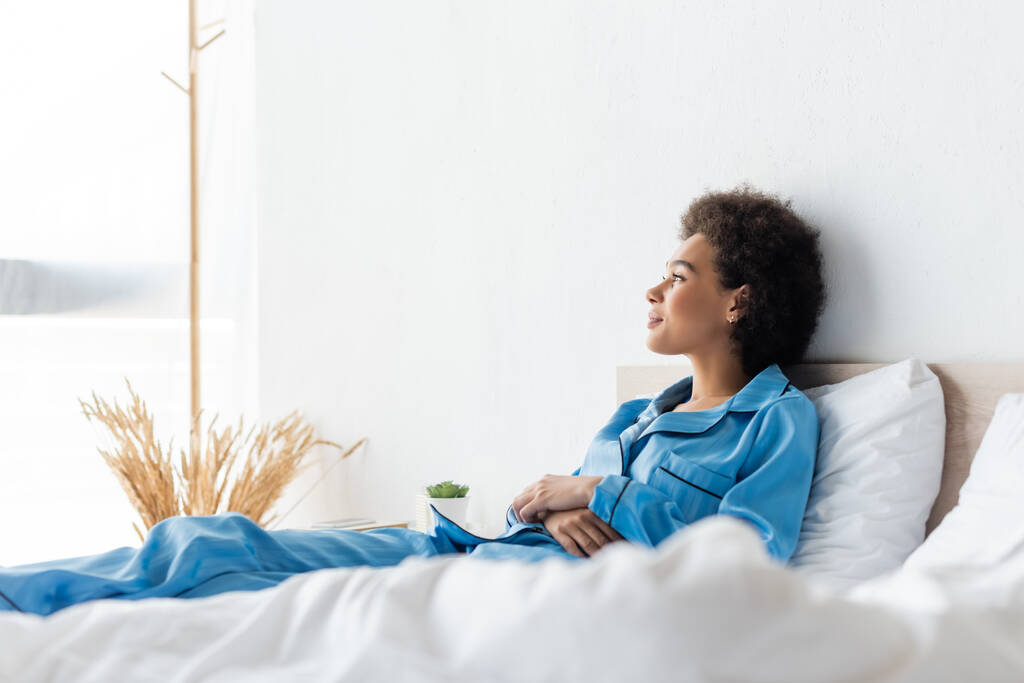 Mutlu Afro-Amerikalı kadın pijamalarıyla yatakta yatıyor. - Fotoğraf, Görsel
