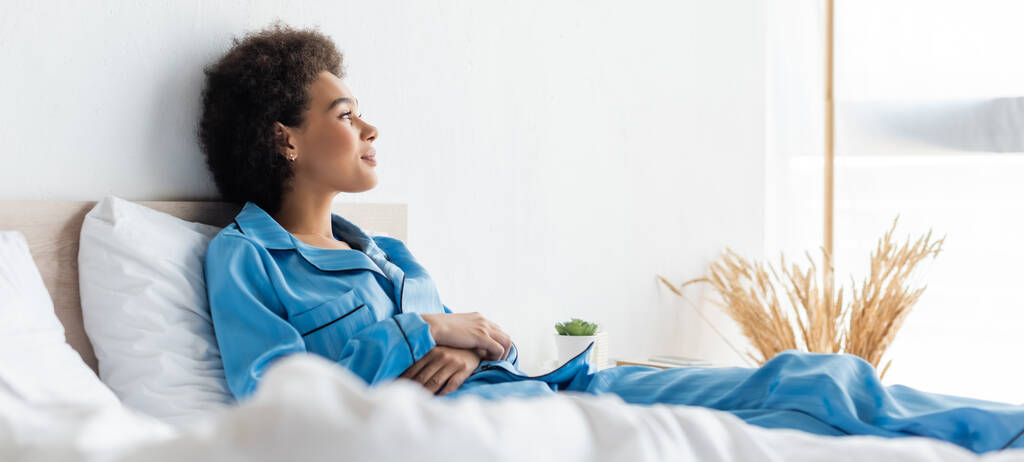 szczęśliwy Afroamerykanka kobieta w piżamie leży na łóżku, sztandar - Zdjęcie, obraz