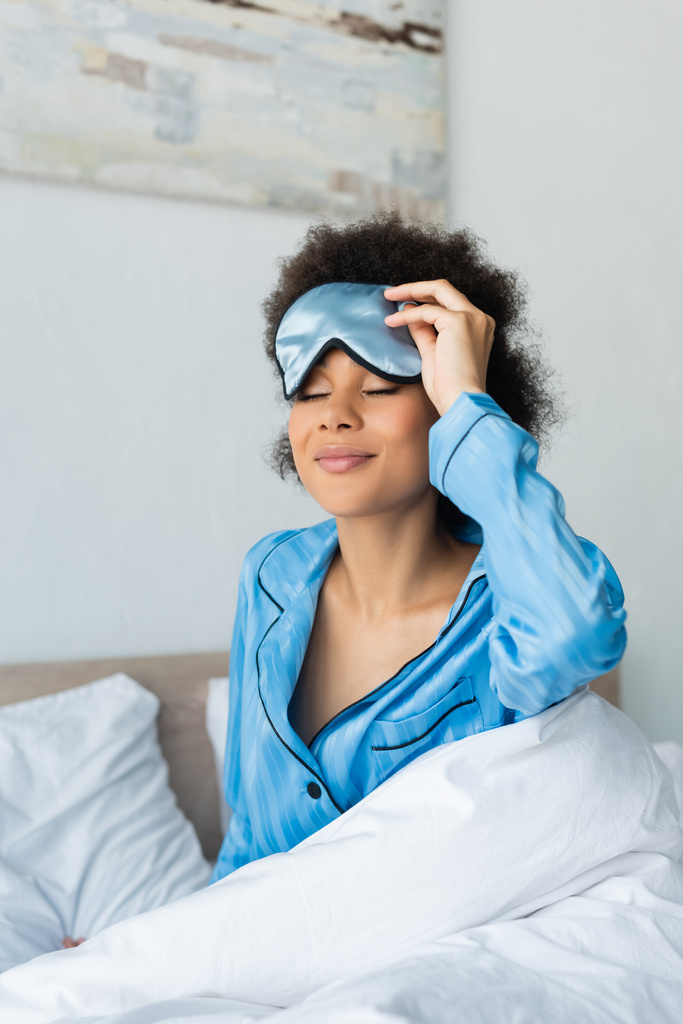 sorrindo mulher americana africana em pijama ajustando máscara de dormir - Foto, Imagem