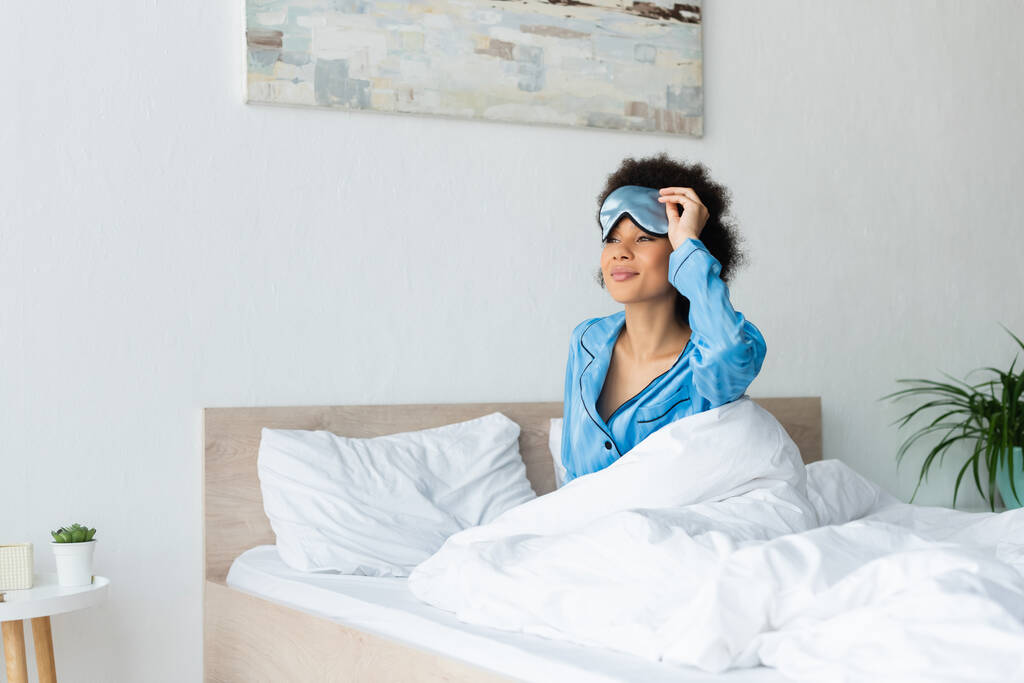 dorminhoco afro-americano mulher em pijama ajustando máscara de dormir - Foto, Imagem