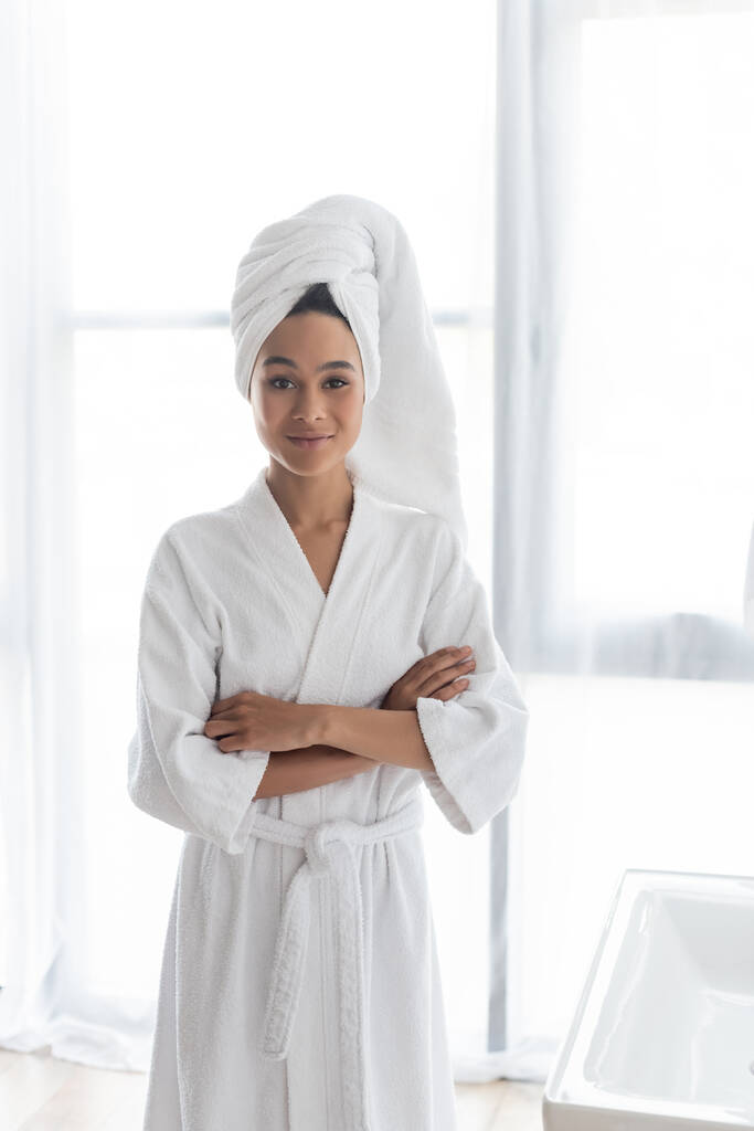 young african american woman in white towel and bathrobe standing with crossed arms - Photo, Image
