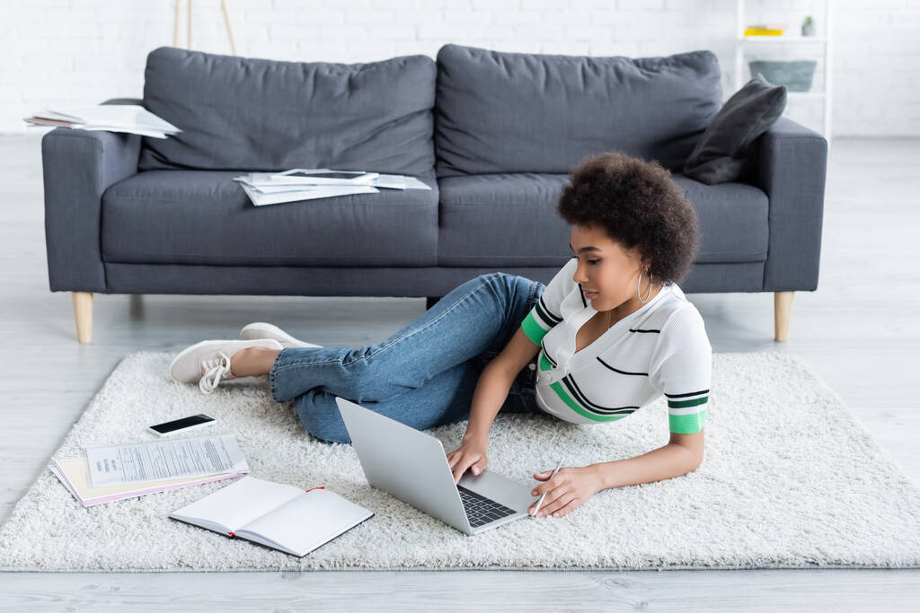 afro-américaine femme en utilisant un ordinateur portable tout en étant couché sur le tapis  - Photo, image