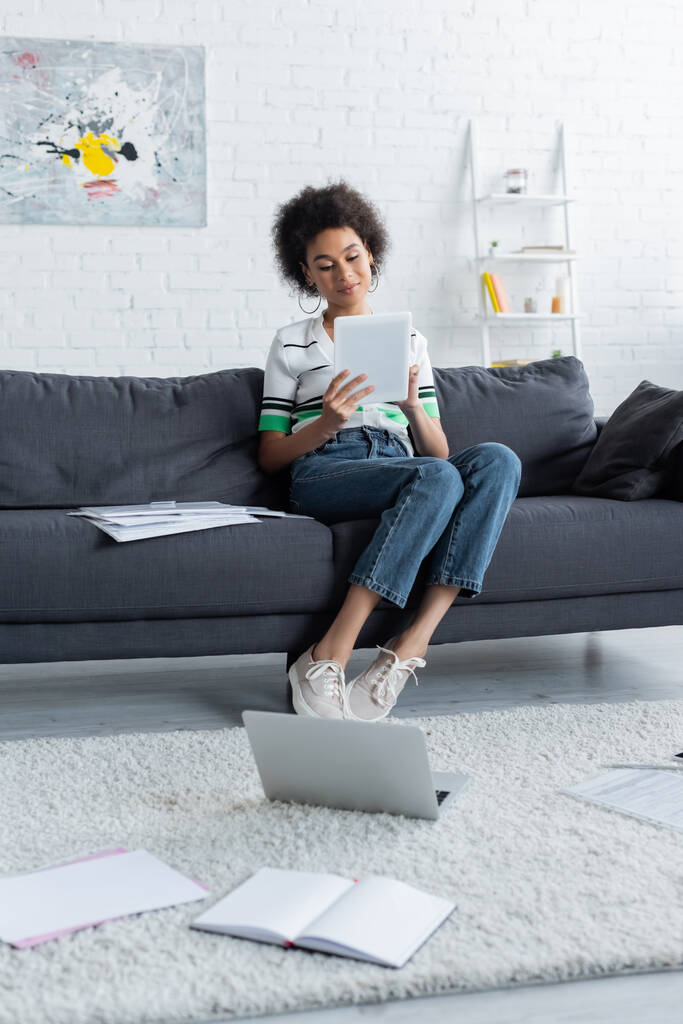mujer afroamericana usando tableta digital mientras está sentada en el sofá  - Foto, Imagen