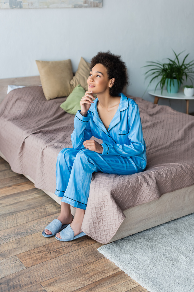 Femme africaine américaine rêveuse assise sur le lit à la maison  - Photo, image