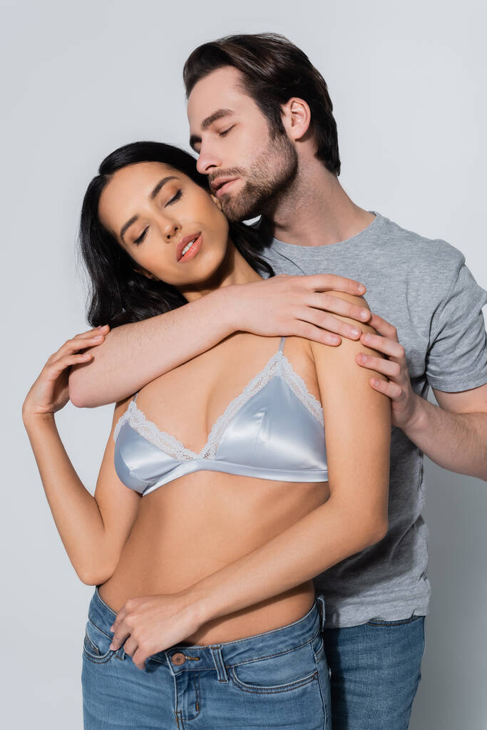 hot woman in satin bra standing with closed eyes near young man seducing her on grey - Photo, Image