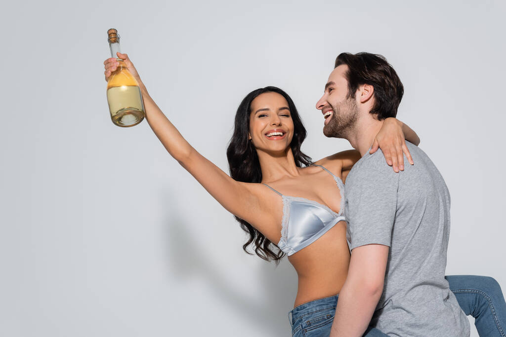 счастливый мужчина в футболке с сексуальной женщиной с бутылкой шампанского на сером - Фото, изображение