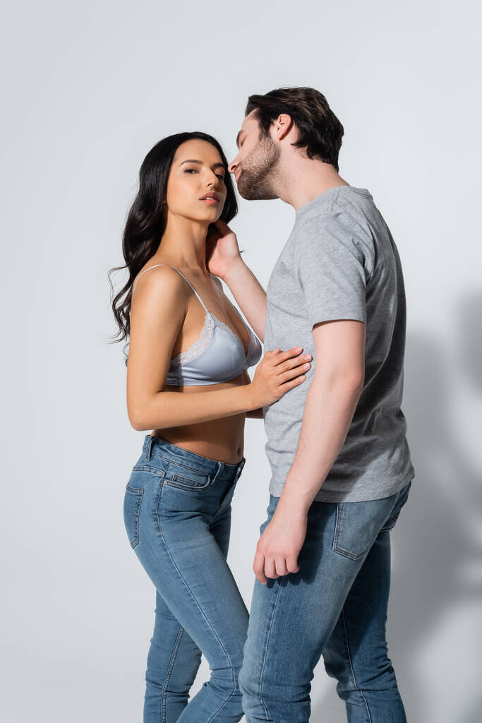 man in t-shirt seducing woman in jeans and bra on grey - Photo, Image