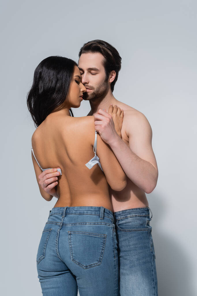 shirtless man with closed eyes taking bra off sexy woman in jeans on grey - Photo, Image