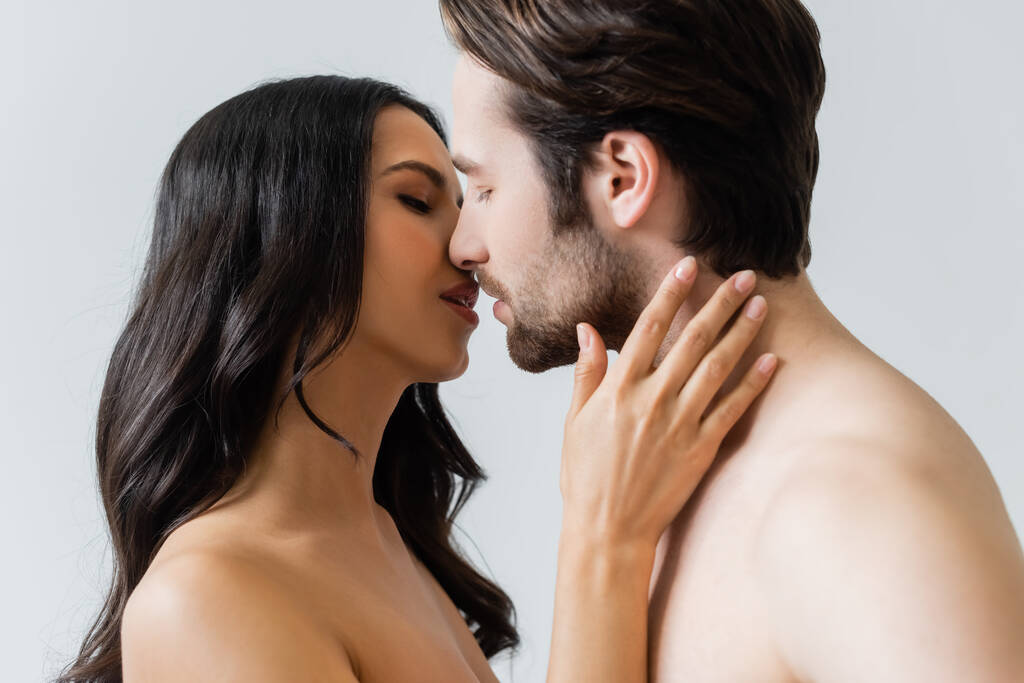 обнаженная брюнетка женщина и мужчина целуются с закрытыми глазами, изолированными на сером - Фото, изображение