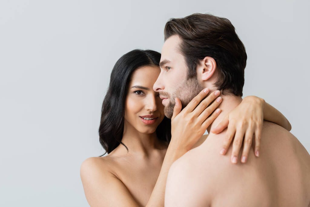 обнаженная женщина смотрит в камеру, обнимая мужчину без рубашки, изолированного от серого - Фото, изображение