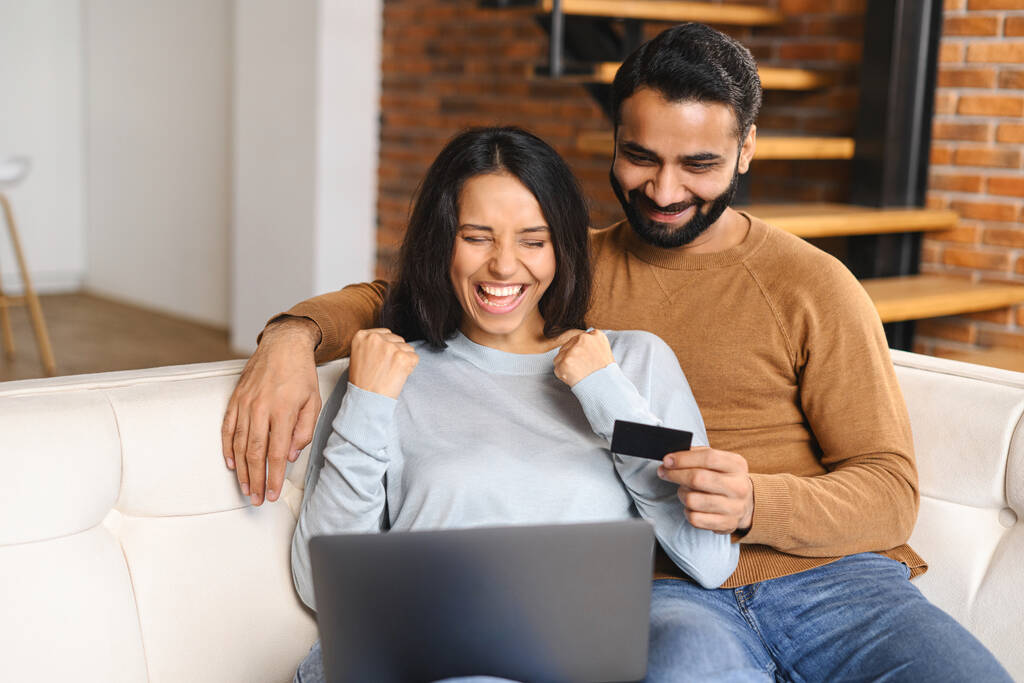 Веселе індійське подружжя дивиться на екран ноутбука і посміхається зубату. Жінка дуже радіє, коли ходить за покупками в Інтернеті зі своїм чоловіком. Передача грошей, онлайн-банкінг - Фото, зображення