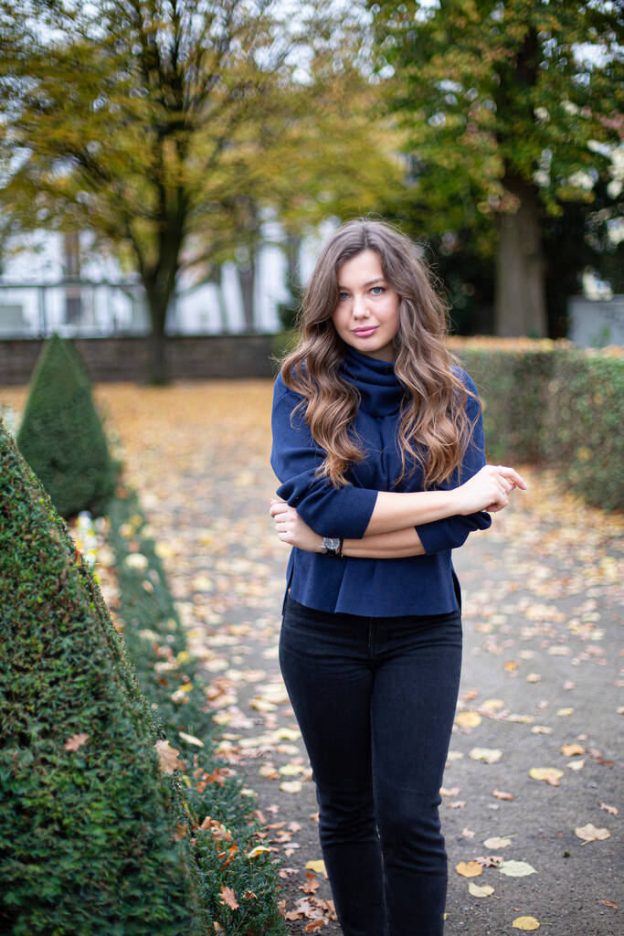 ładna młoda Europejka w ciemnoniebieskim swetrze z długimi kręconymi włosami w jesiennym parku - Zdjęcie, obraz