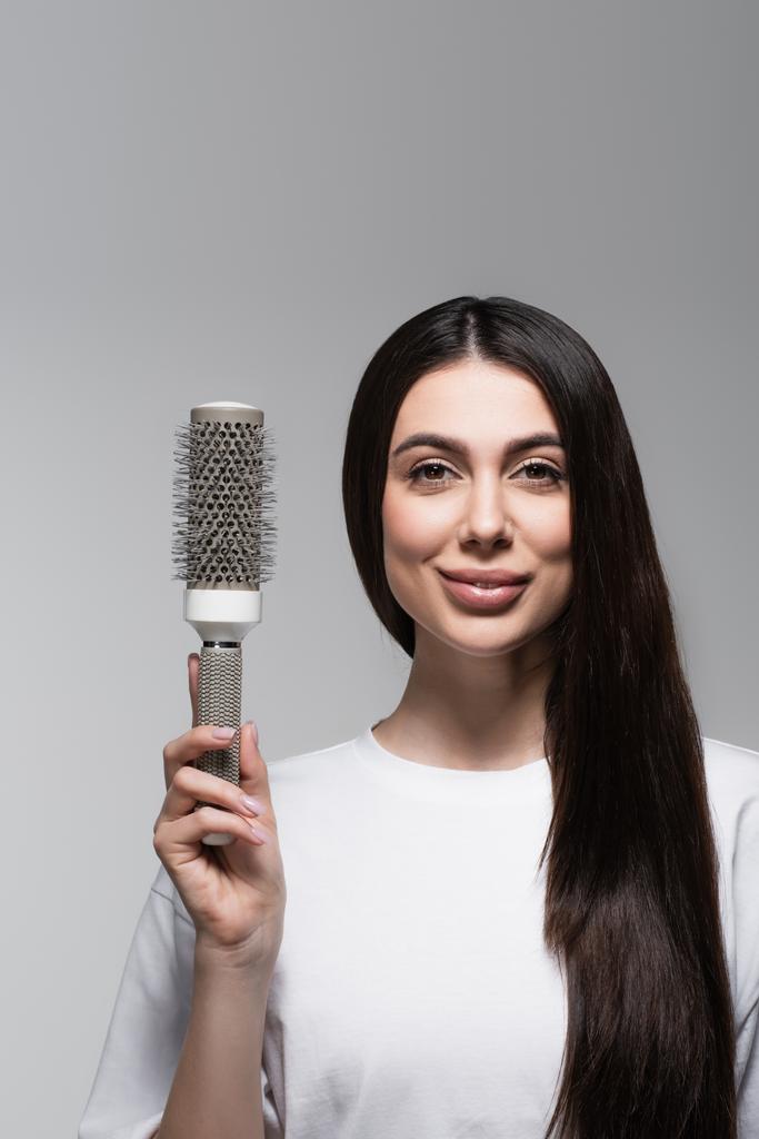mulher satisfeita com cabelo longo liso segurando escova térmica isolada em cinza - Foto, Imagem
