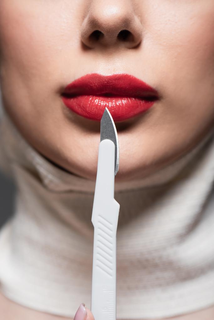 Ausgeschnittene Ansicht einer jungen Frau mit roten Lippen in der Nähe eines scharfen Chirurgenmessers - Foto, Bild