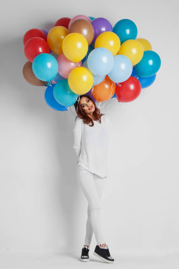 Volledige lengte van een gelukkige vrouw houden ballonnen tegen witte achtergrond - Foto, afbeelding