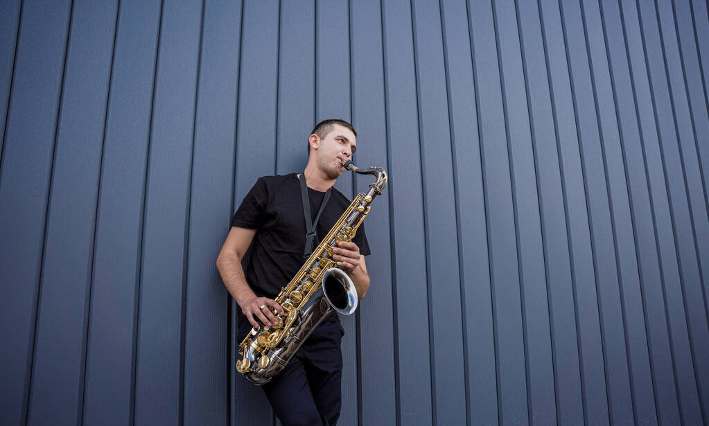 Jeune musicien de rue jouant du saxophone près du grand mur bleu - Photo, image