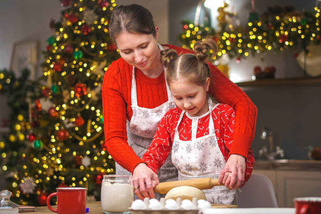 Καλά Χριστούγεννα. Η κόρη μου βοηθάει τη μητέρα μου να μαγειρέψει. Οικογενειακή μαγειρική εορταστικού φαγητού. Η μητέρα και η κόρη φτιάχνουν χριστουγεννιάτικα μπισκότα. Καλές γιορτές. Βραδινή ώρα, ευτυχισμένη οικογένεια στην κουζίνα. - Φωτογραφία, εικόνα