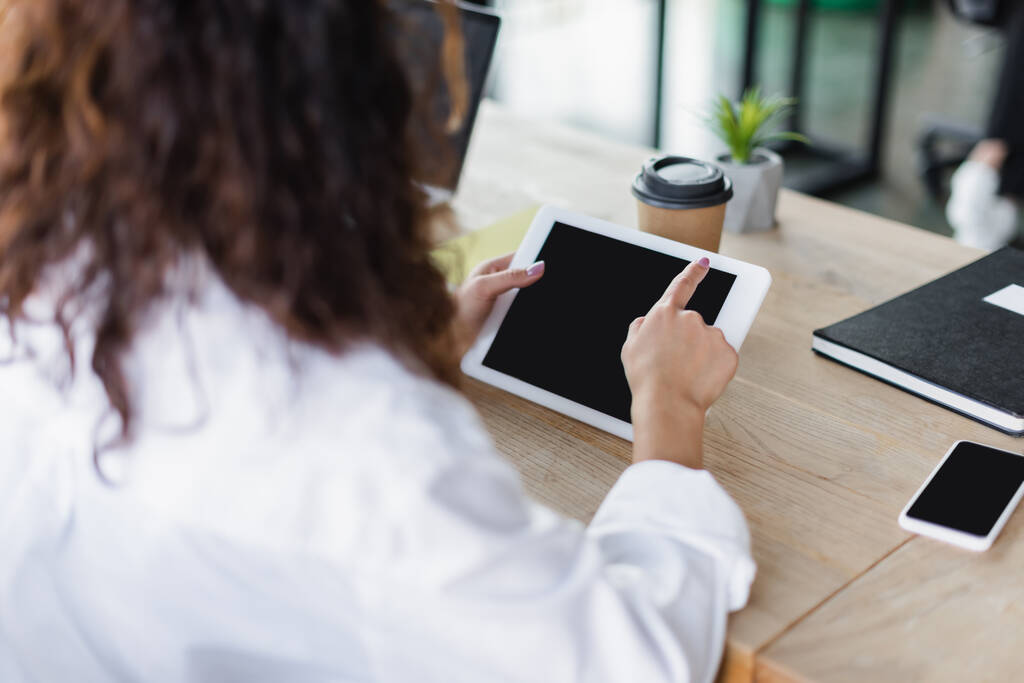 vista recortada de la mujer borrosa utilizando tableta digital con pantalla en blanco cerca de teléfono inteligente y café para ir en el escritorio - Foto, imagen