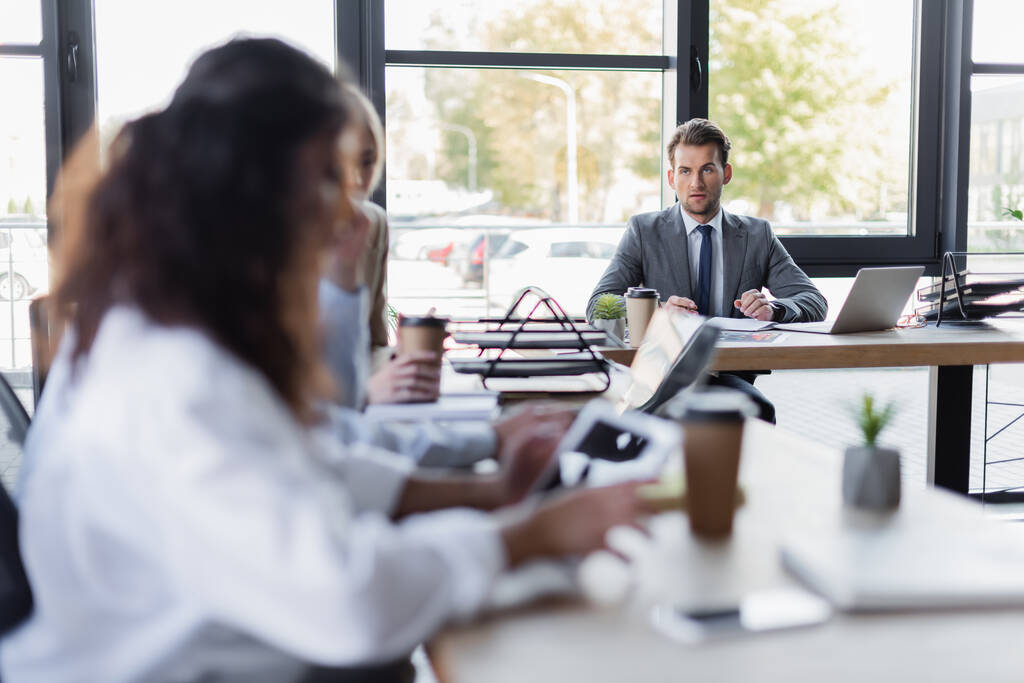 blurred businesswomen sitting at desk near young businessman in formal wear - Foto, immagini