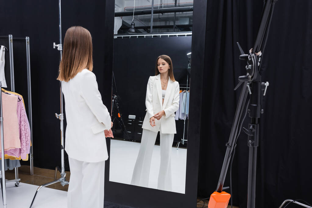 профессиональная модель в белом стильном костюме, стоящая возле зеркала в гримерке - Фото, изображение