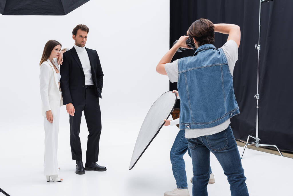modelos jóvenes y elegantes posando cerca de fotógrafo y asistente en estudio de fotografía - Foto, imagen