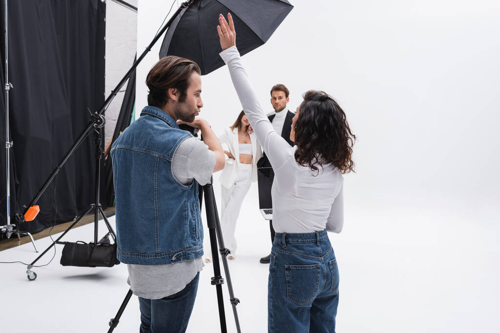 art director standing with raised hand while talking to photographer near models in photo studio - Photo, Image
