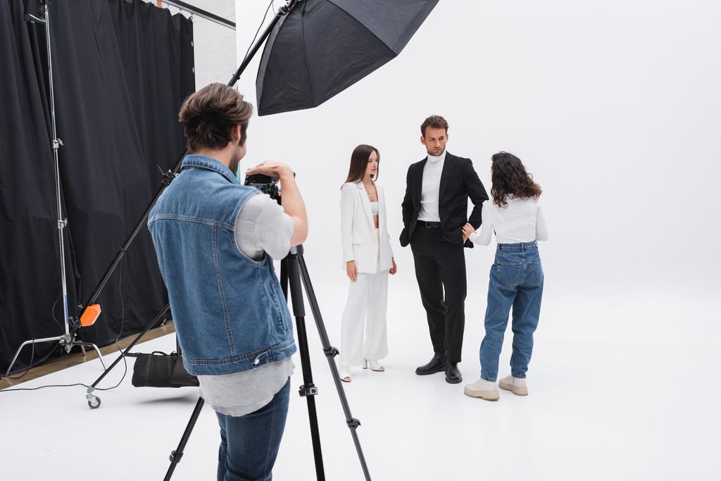 fotograaf aanpassen digitale camera terwijl art director praten met modellen in fotostudio - Foto, afbeelding