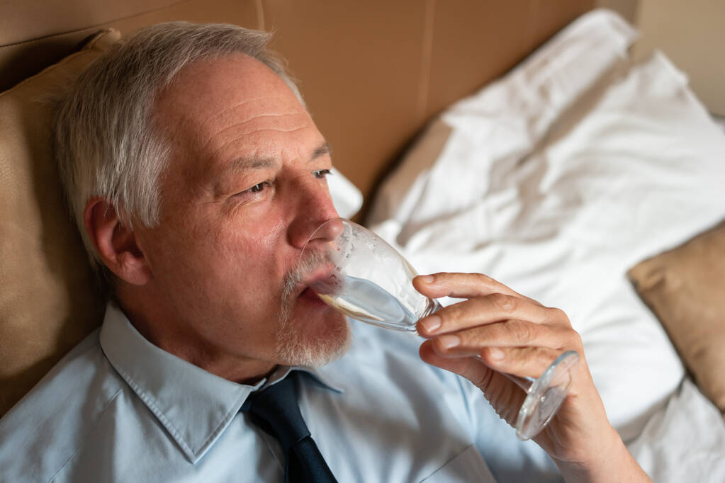 Droevige zakenman drinkt wijn alleen in zijn slaapkamer, verdriet en stress concept - Foto, afbeelding