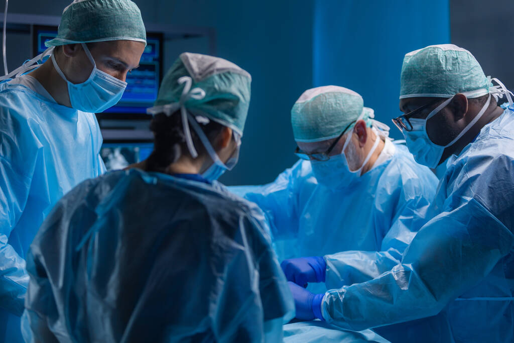 Wielorasowy zespół profesjonalnych lekarzy wykonuje operację chirurgiczną w nowoczesnym szpitalu. Lekarze pracują nad ratowaniem pacjenta. Medycyna, zdrowie, kardiologia i transplantacja. - Zdjęcie, obraz