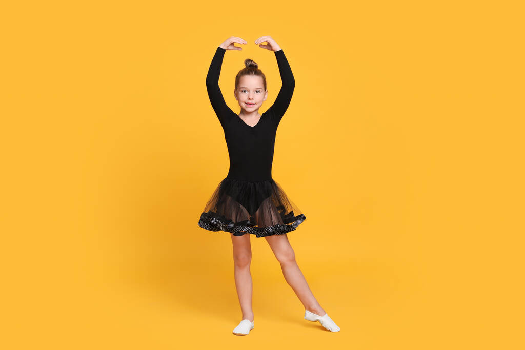 Carino bambina in abito nero ballare su sfondo giallo - Foto, immagini